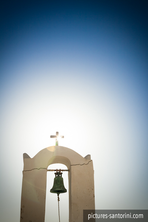A bell tower in Fira, Santorini, photographed against the afternoon sun and deep blue sky