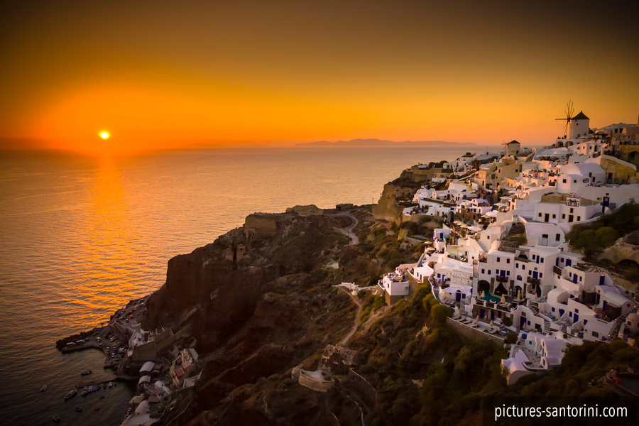 The sun setting beyond Oia, Santorini, as the village gathers above the caldera for the evening light