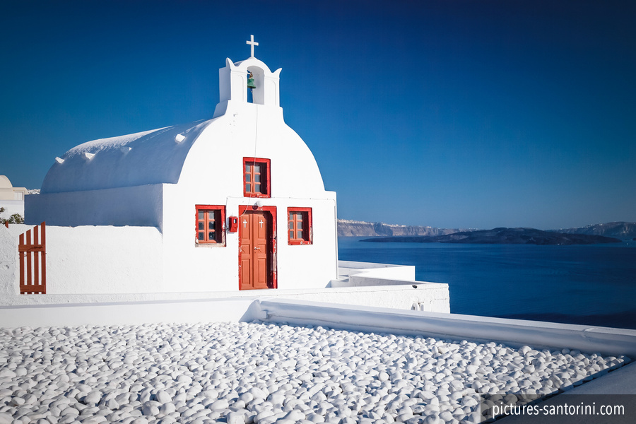 A small white chapel in Oia, Santorini, standing against the deep blue Aegean Sea