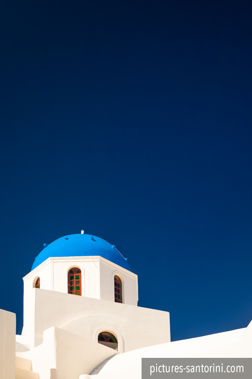 One of the many blue domed churches in Santorini in front of the deep blue sky. This particular church is situated in Oia