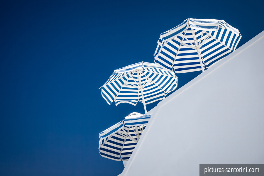 Sun umbrellas striped in blue and white against a deep blue sky. Picture was taken in Imerovigli, Santorini